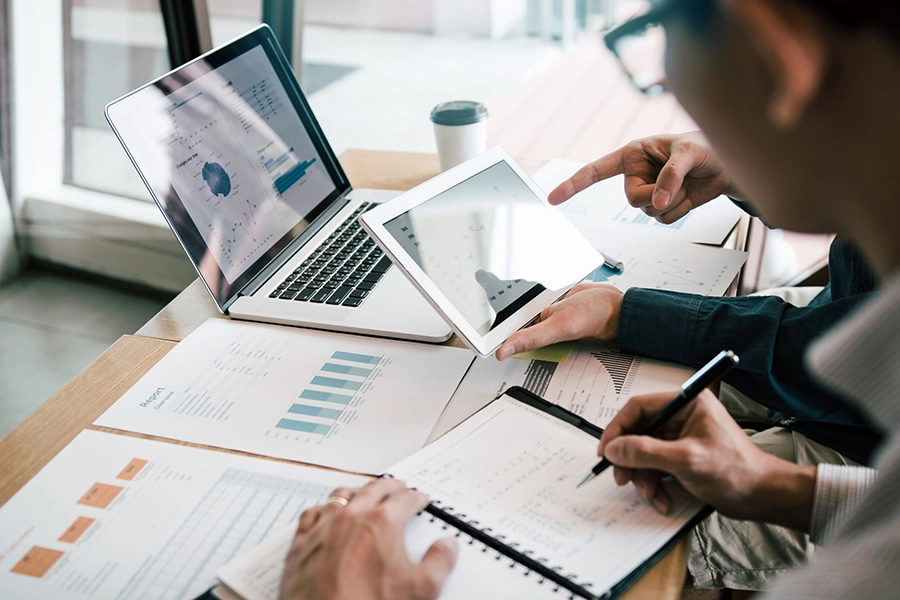 Business Analytics and Strategic Planning Review Business professionals analyzing financial reports, performance metrics, and growth strategies on laptops and documents.